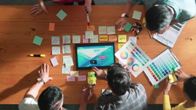 Top view of skilled business people working together to design web design. Aerial view of designer brainstorming and discussing about website interface for computer or digital application. Symposium.