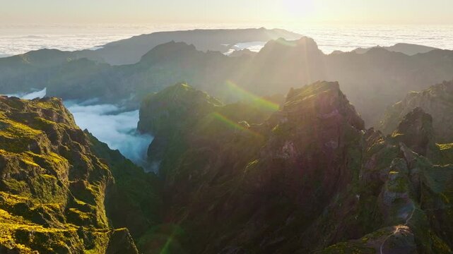 Aerial view at Pico do Arieiro of mountains over clouds with blooming Cytisus shrubs on sunset with sunburst. Madeira island, Portugal. Orbit parallax shot