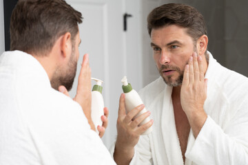 Beauty, skincare and man with cream on face using skincare products, lotion. Closeup of male face. Men's beauty. man is applying moisturizing and anti aging cream on his face against white background.