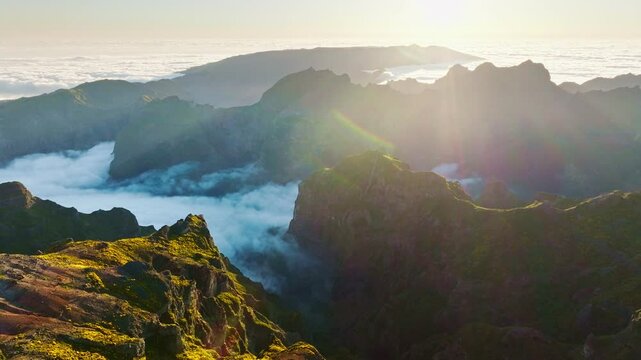 Aerial view at Pico do Arieiro of mountains over clouds with blooming Cytisus shrubs on sunset with sunburst. Madeira island, Portugal. Pull away out dolly retreat shot