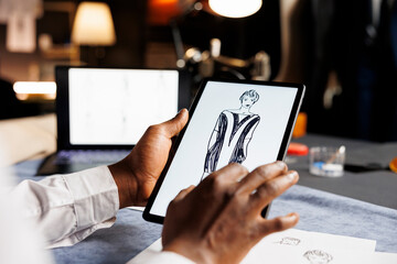 Couturer meticulously analyzing drawn sketch designs on tablet of exquisite dress comissioned by...