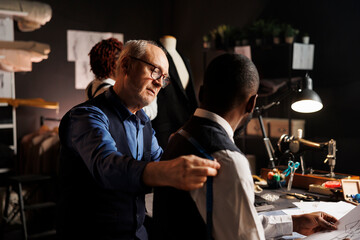 African american apprentice suitmaker helping master fashion designer with sartorial piece measurements in studio workspace. Experienced craftsman checking bespoken suit fitting assisted by couturier