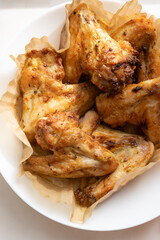 Freshly fried chicken wings are placed on paper in white plate. Homemade meal cooked in air fryer grill. Selective focus, vertical photo