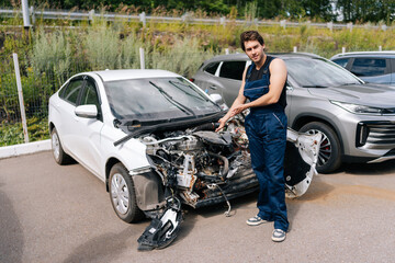 Serious mechanic assessing damage to white car that has been severely damaged in accident, front...