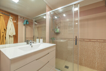 A conventional bathroom with a flat-floor shower cabin, frameless mirror on the wall, mosaic tiles and cream colour