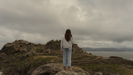 Woman observing the ancient Castro de Baroña ruins on a cloudy day