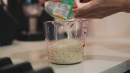 Woman measures rice with measuring jug in kitchen on a bright day