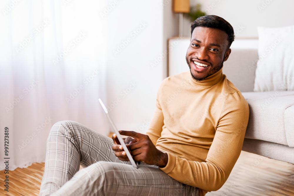Aufkleber Black Guy Using Tablet Computer Smiling At Camera Sitting On Floor At Home. Selective Focus