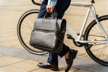 Professional Individual Carrying a Black Briefcase While Walking Beside a Bicycle in an Urban...