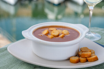 Homemade tasty fish or bisque soup with croutons served with glass of cold white wine and view on yacht boats and houses of Port Grimaud, French Riviera, France. Food of Provence