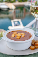 Homemade tasty fish or bisque soup with croutons served with glass of cold white wine and view on yacht boats and houses of Port Grimaud, French Riviera, France. Food of Provence