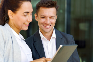 Obraz premium Two Professionals Engaged in a Discussion While Reviewing a Tablet Outdoors During a Sunny Day in an Urban Setting