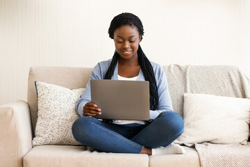 Naklejka premium Freelance concept. African american millennial woman working with laptop computer on sofa at home