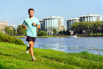 Man Jogging Along a Riverside Park With Modern Buildings in the Background During a Clear and Sunny Day