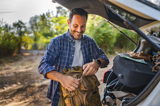 Adult man take backpack from trunk ready for adventure in the forest