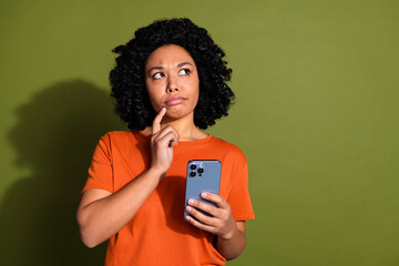 Photo of lovely young lady hold device look skeptical empty space dressed stylish orange garment...
