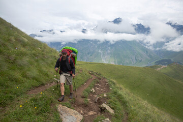 Obraz premium A hiker pauses on a mountain trail, carrying a large pack, with majestic peaks shrouded in mist behind him