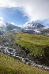 Fototapeta premium A breathtaking alpine landscape with a glacier, lush green meadows, and a small building. Mount Kazbek or Kazbegi, the Caucasus, Georgia
