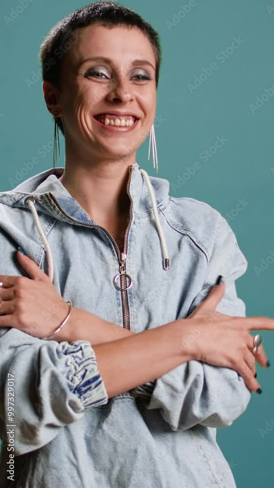 Poster Vertical video Trendy millennial woman smiling with confidence against blue background, feeling happy and pleased with her stylish outfit and make up look. Female model dressed in street style. Camera