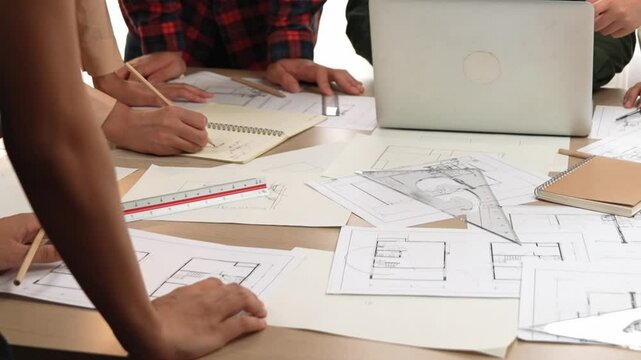 Architect and safety engineer discussion about building blueprint displaying on laptop on table with architectural document and wooden block scatter around at modern office. Closeup. Delineation.