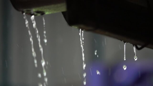 A pipe is dripping water in the rain. The water is falling in a steady stream. Concept of calmness and tranquility