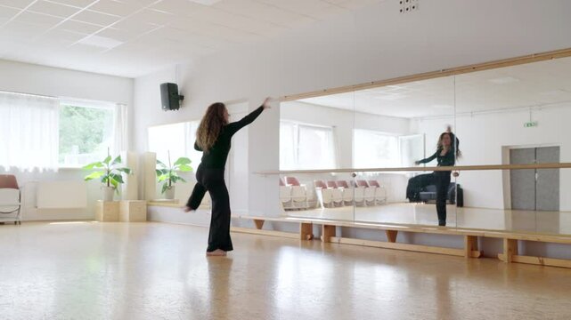Gracefully woman in black outfit active dancing modern dance in bright room. Her curly hair flows freely and her face radiates happiness and energy embodying essence of movement and freedom. 4K video.