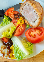 Traditional Pork Pie,close-up and cut into segments with a backdrop of English mustard,sweet pickle and salad.