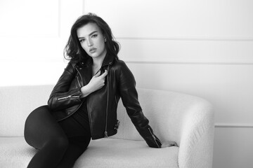 A stylish woman poses in a black leather jacket against a white background