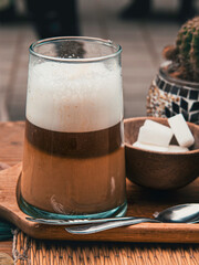 Traditional Moroccan layered 'Nous Nous' coffee beverage with creamy foam in a glass, served with sugar cubes on a rustic wooden tray – cozy outdoor café scene in Essaouira, Morocco