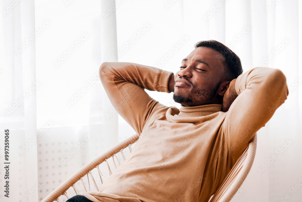 Aufkleber weekend at home. lazy black guy relaxing sitting on modern chair against window indoor. selective fo