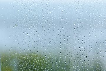 Rainy day with droplets on a windowpane, creating a blurred view of greenery outside during...