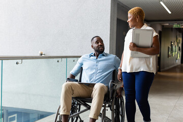 Obraz premium Colleagues discussing work, african american man in wheelchair holding tablet, woman carrying laptop