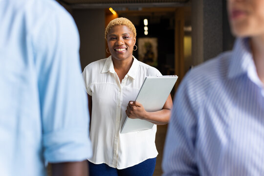 Smiling woman holding laptop, walking and engaging with colleagues in office