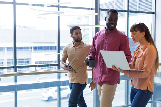 Discussing work, diverse colleagues using laptop and tablet in modern office, copy space
