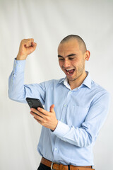 Surprised and joyful young businessman raising his fist and with the other holding his smartphone