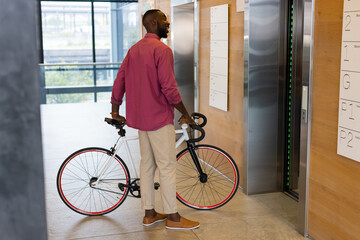 Fototapeta premium Man holding bicycle waiting for elevator in modern office building lobby