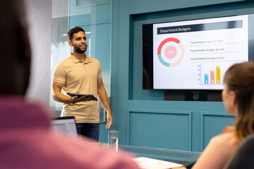 Holding tablet and explaining charts, man presenting department budgets in meeting room