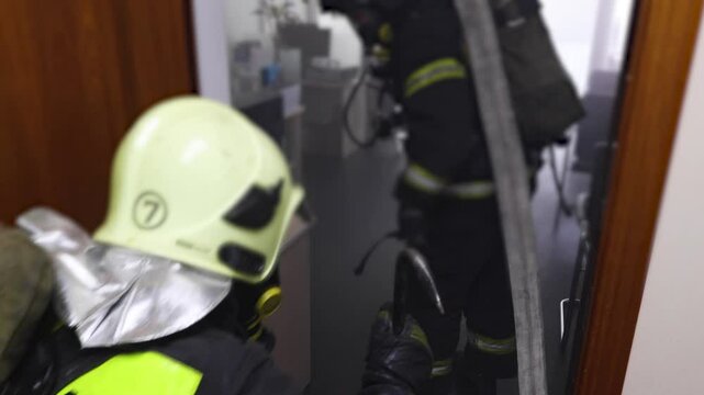 Group of firefighters in protective uniform during fire fighting operation inside the office building corridor, firemen brigade during fire drill, emergency and rescue service, exercise and training