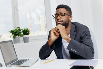 Contemplative african american man sitting at a desk with his hand on his chin, deep in thought