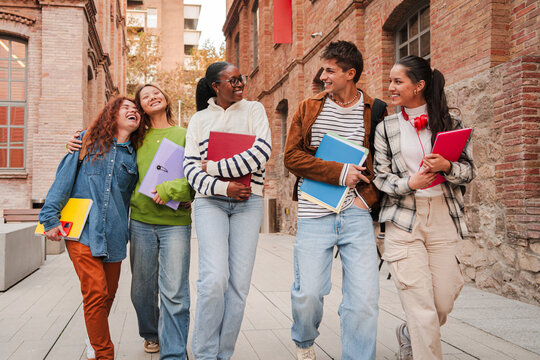 Group of diverse students walking together on campus, smiling and carrying notebooks, highlighting friendship, education, and student life in a university setting. Classmates enjoying school together
