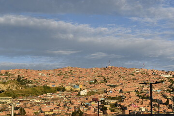 A panoramic photograph of an empty parking lot beneath a clear blue sky, with a hillside of houses in the background. The image captures an open urban space, providing a calm and traffic-free atmosphe