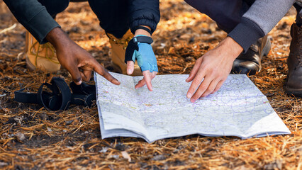 Backpackers pointing at map, looking for their location at forest, closeup