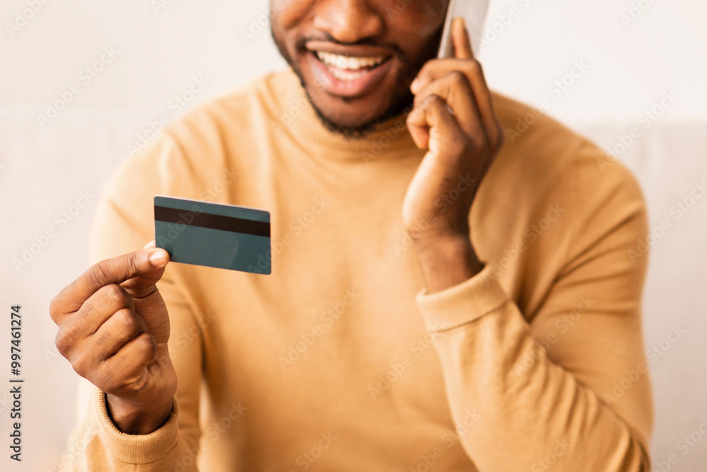 Poster Online Banking. Happy Afro Man Using Credit Card And Laptop Talking On Phone Sitting On Couch At Home.