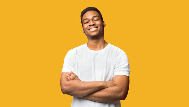 Confident Guy. Happy black man looking at camera with crossed arms folded, panorama, copyspace, orange wall