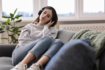 Obraz premium Loneliness concept. Sad teenage girl in headphones listening to music on sofa at home