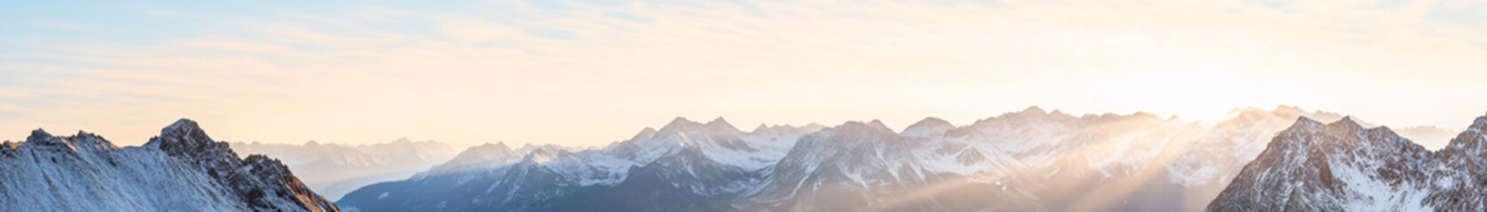 A breathtaking panoramic shot of a majestic mountain range, where the rugged terrain is visible in extraordinary detail. The sharp, snow-dusted peaks rise steeply, with every rock face and snow drift
