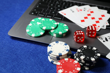 Poker chips, laptop, playing cards and dices on blue table. Online game