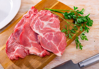 Slices of fresh raw pork loin head with fat marbling, prepared for roasting on wooden board, placed...