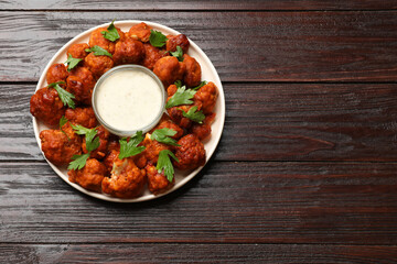 Baked cauliflower buffalo wings with parsley and sauce on wooden table, top view. Space for text