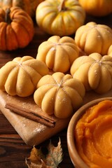 Raw pumpkin shaped buns and ingredients on wooden table, closeup